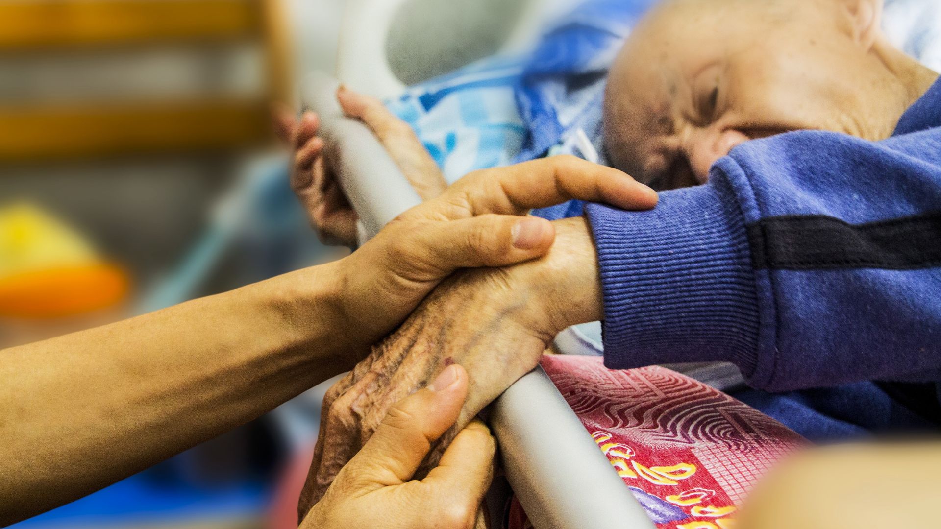 Caring hands holding elderly person's hand in hospital or care setting