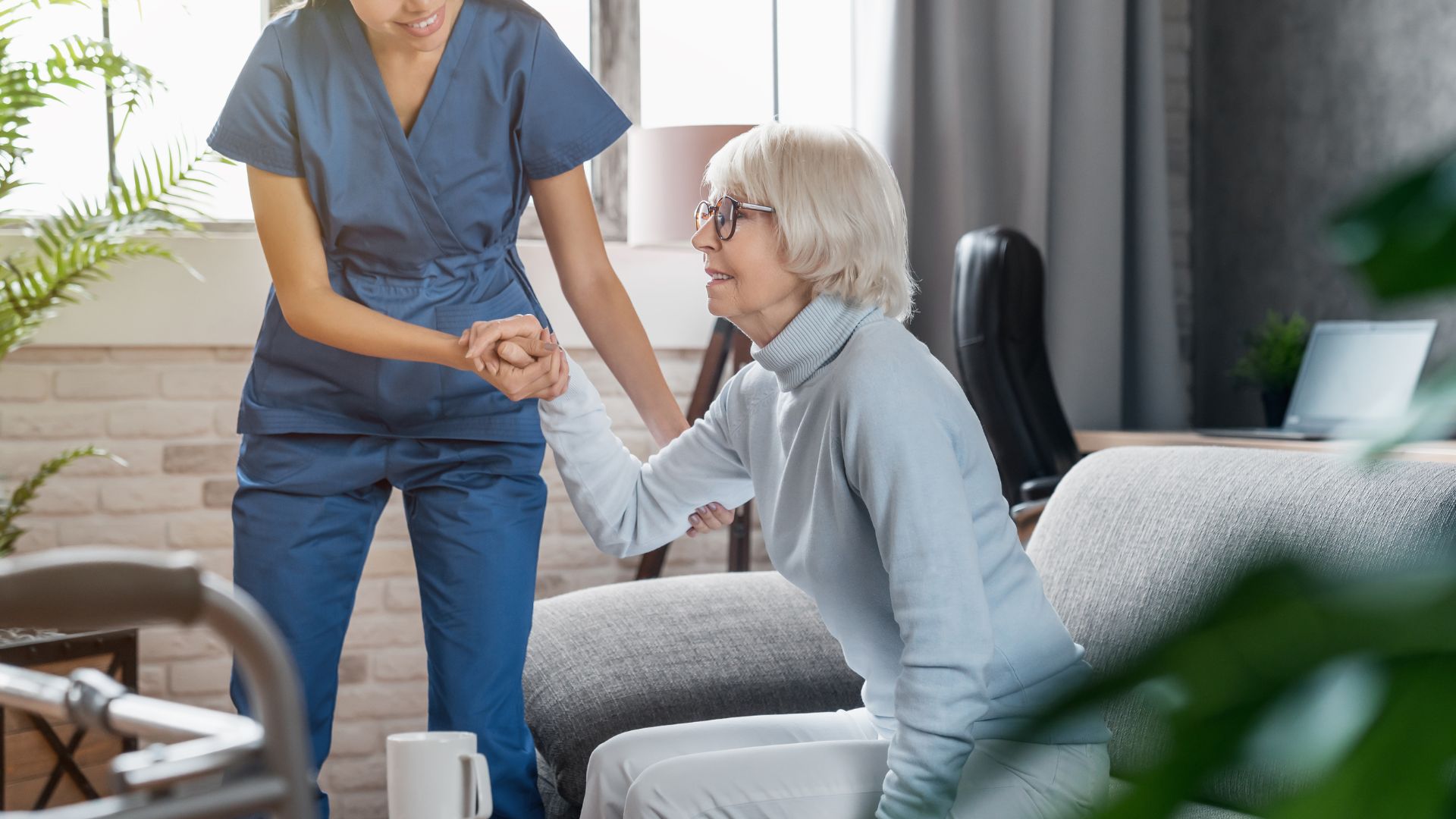 Nurse helping elderly woman stand up in comfortable home setting