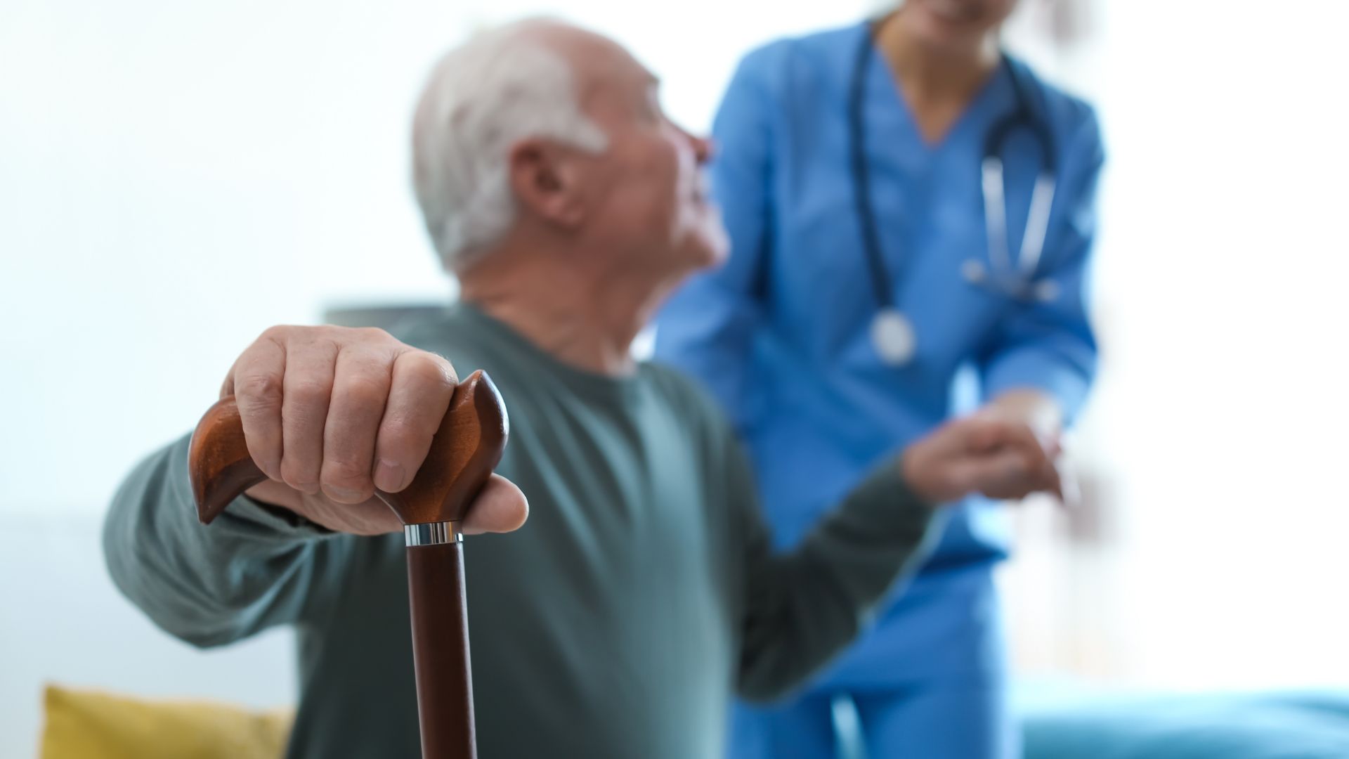 Elderly patient with walking cane receiving medical care from healthcare professional