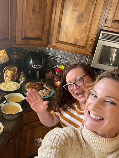 Two smiling friends cooking together in a cozy kitchen with wooden cabinets
