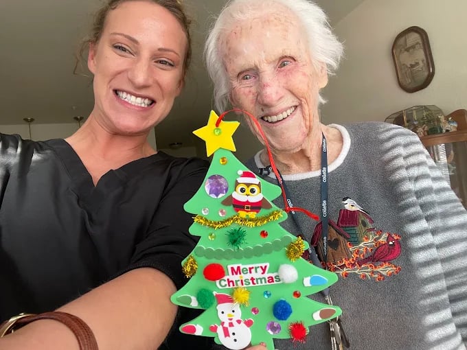 Older and younger woman smiling together with a decorated Christmas tree