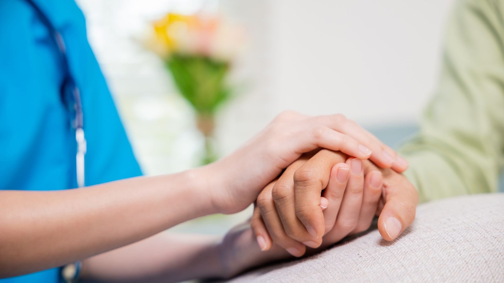 Healthcare worker gently holding patient's hand with compassion